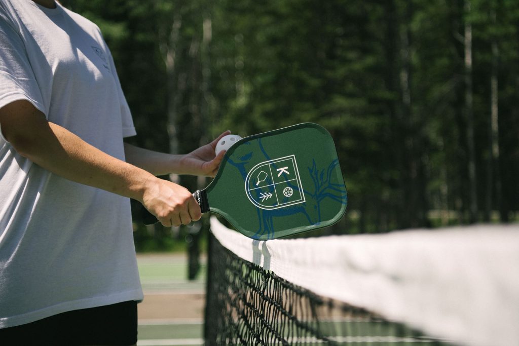 Person holding Pomeroy Kananaskis Mountain Lodge branded pickleball raquet